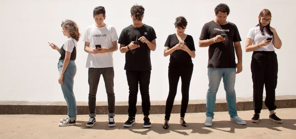 A group of people are standing next to each other looking at their phones.