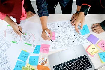 A group of people are sitting around a table with sticky notes and a laptop.