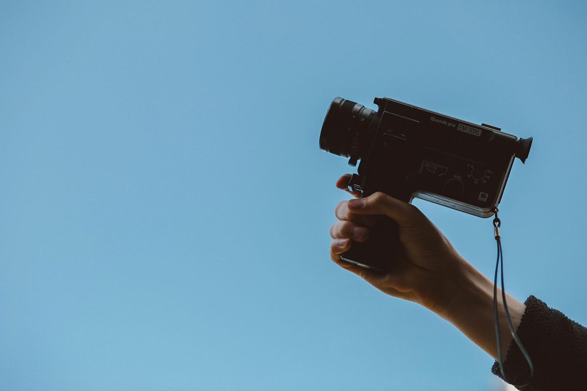 Hand holding a small black camcorder against a clear blue sky