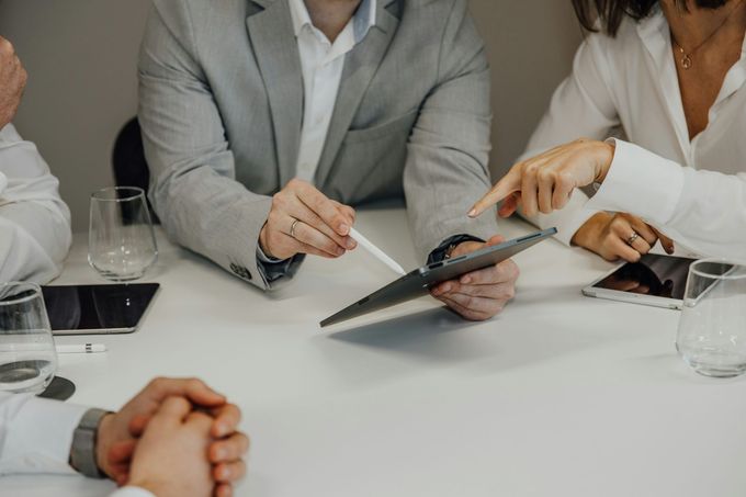 People in business attire at a table, looking at a tablet, pointing.