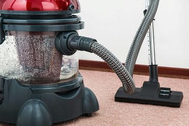 A red and black wet/dry vacuum cleaner with hose and nozzle on a pink carpet.