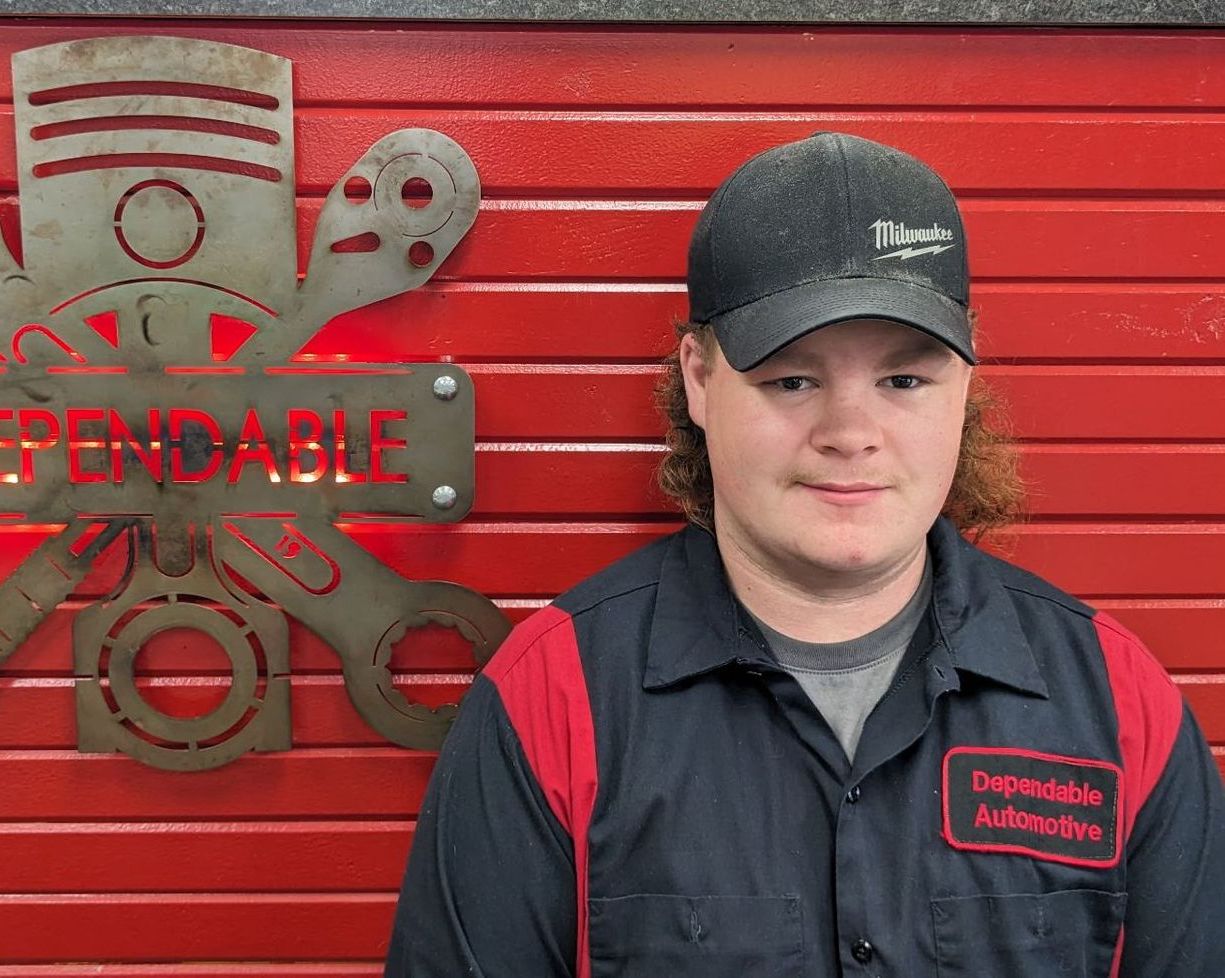 Person in black and red uniform standing before a red garage door with a fire department emblem. | Dependable Automotive