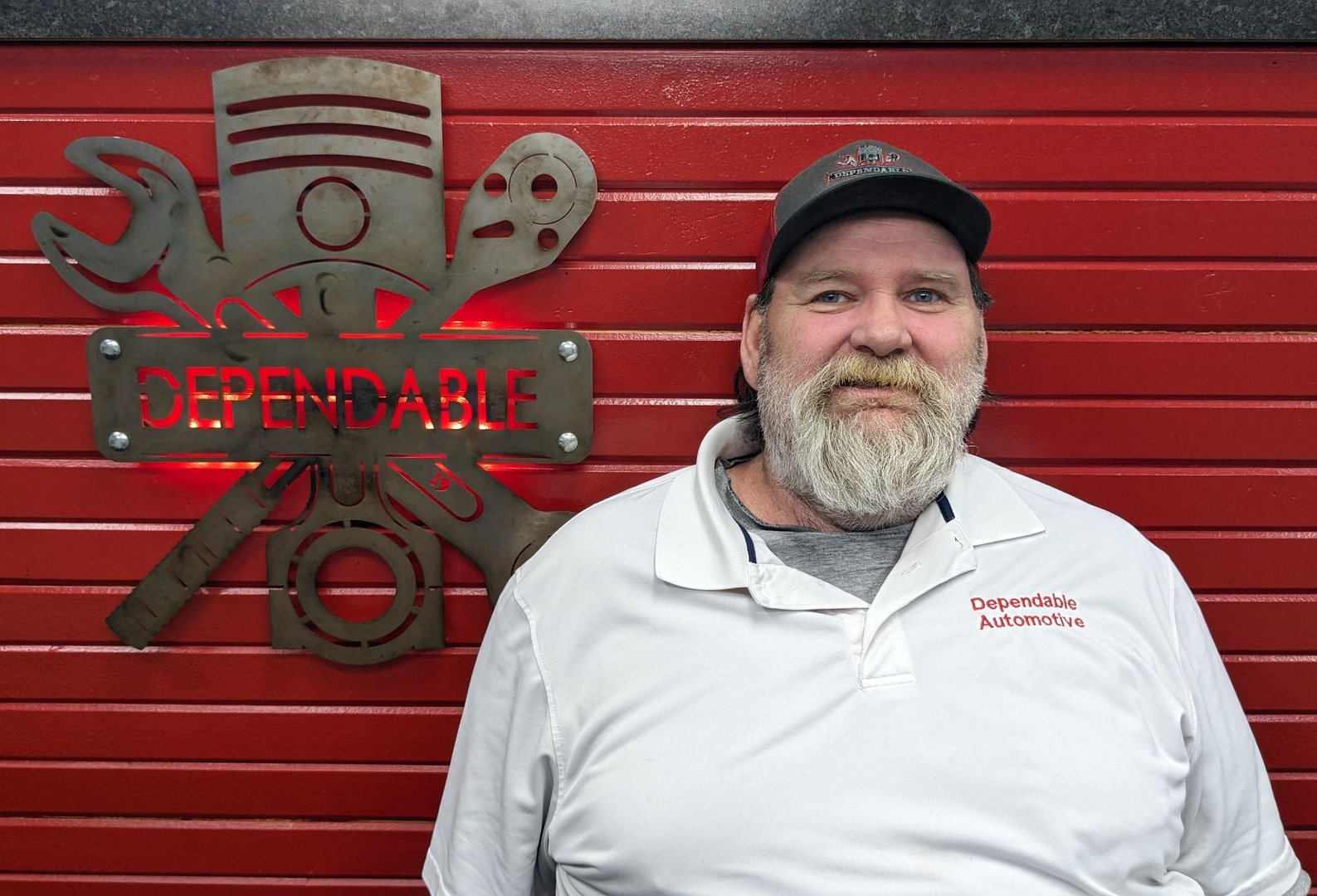 Man in white polo and cap standing by a red wall with the Expedable logo sign | Dependable Automotive