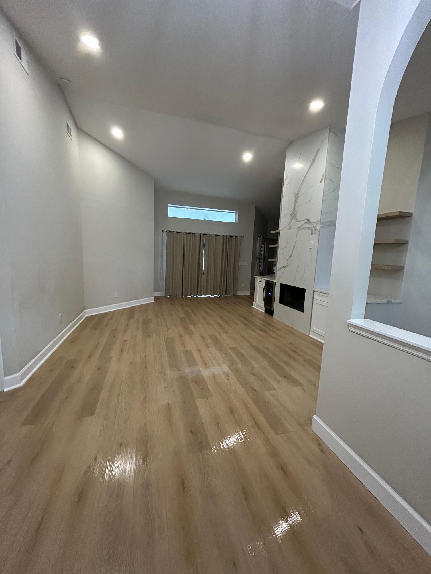 Spacious living room with light wood floors, a fireplace, and neutral-colored walls.