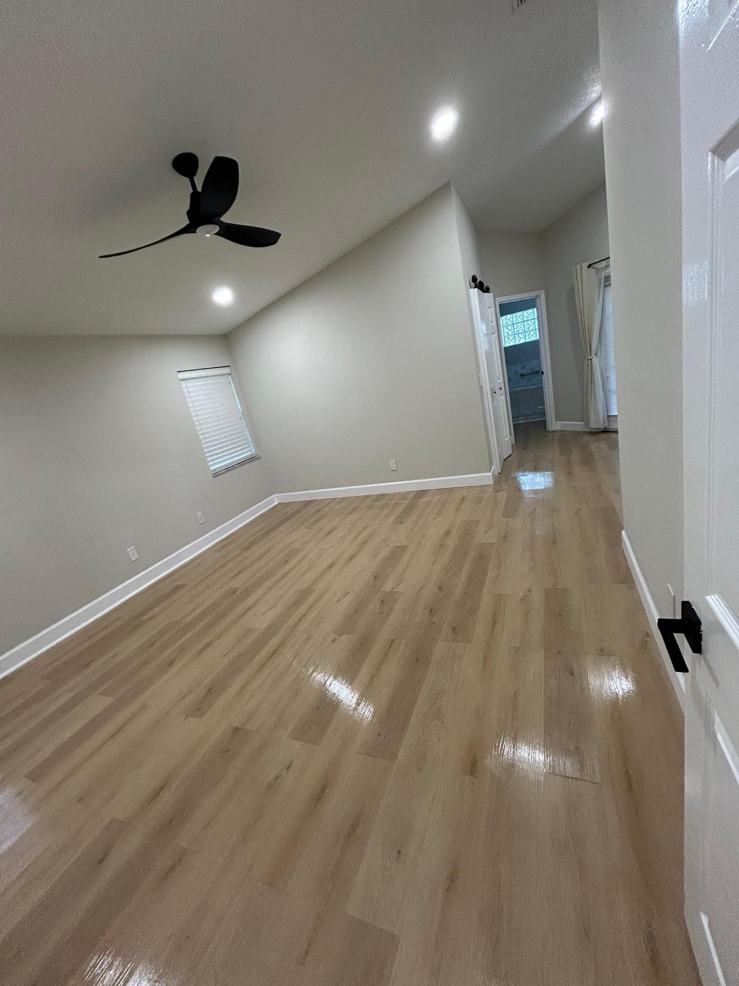 Empty room with wood floors, a ceiling fan, and access to a hallway.