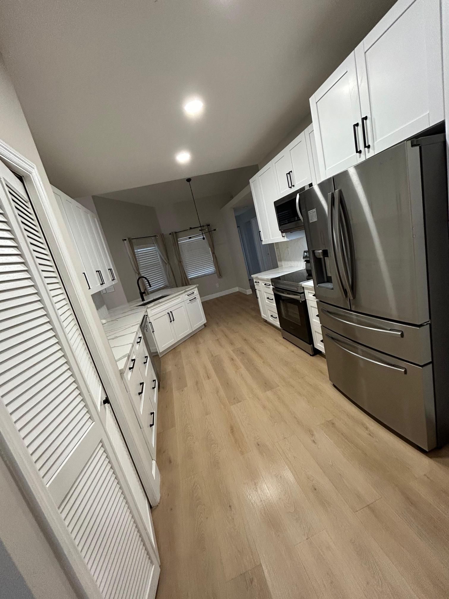 Modern kitchen with white cabinets, stainless steel appliances, and wood-look flooring.