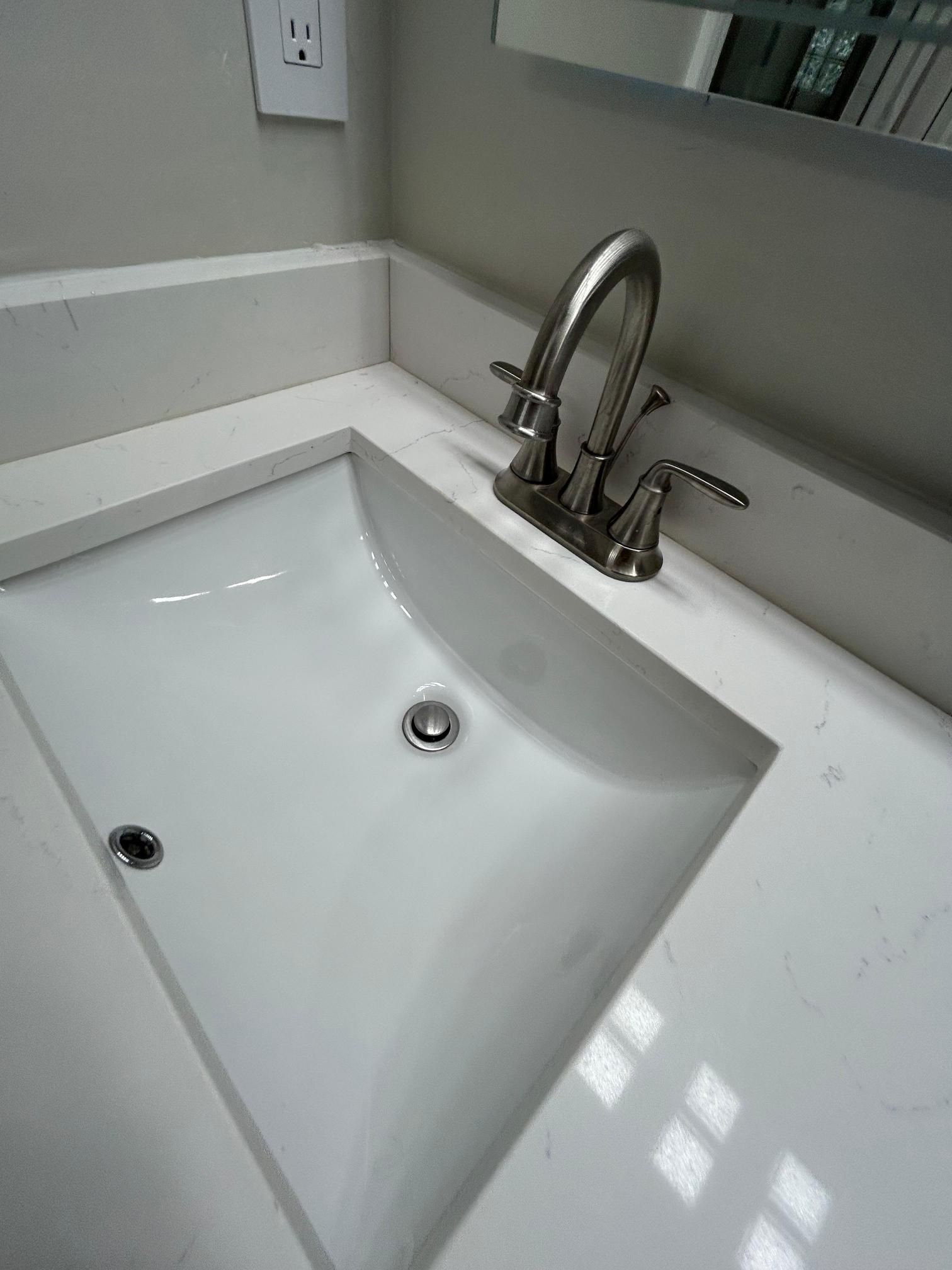 White bathroom sink with a chrome faucet on a white countertop.