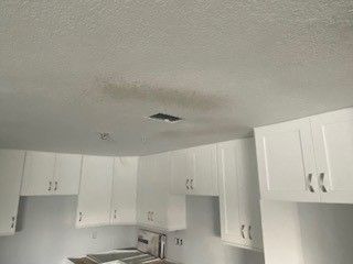 A kitchen with white cabinets and a ceiling with a hole in it.