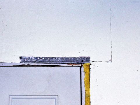 A man is installing drywall on a wall in a room.