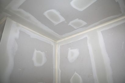 A corner of a room with drywall walls and a ceiling.