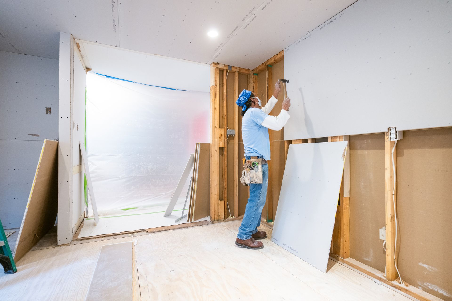 A man is installing drywall on a wall in a room.