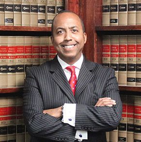 A man in a suit and tie is standing in front of a bookshelf filled with books.
