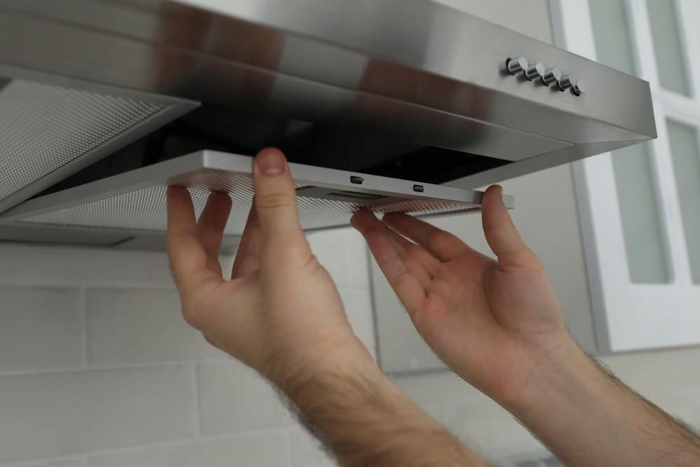 A person is fixing a stainless steel hood in a kitchen.