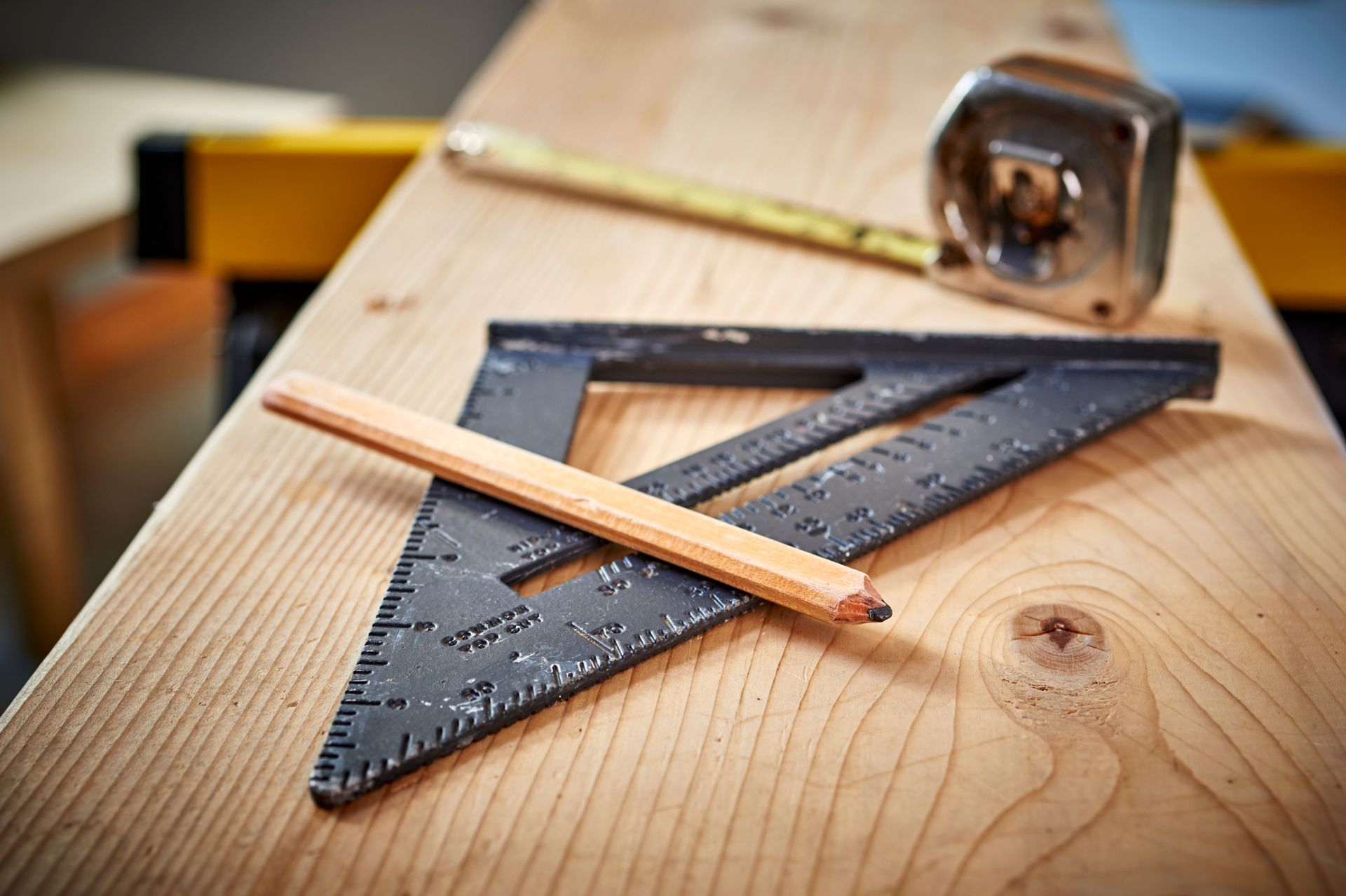 A triangle , pencil and tape measure are on a wooden table.