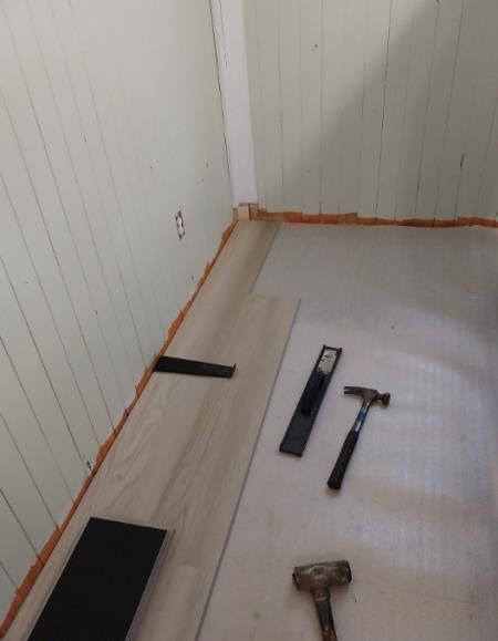 A man is kneeling down to install a wooden floor