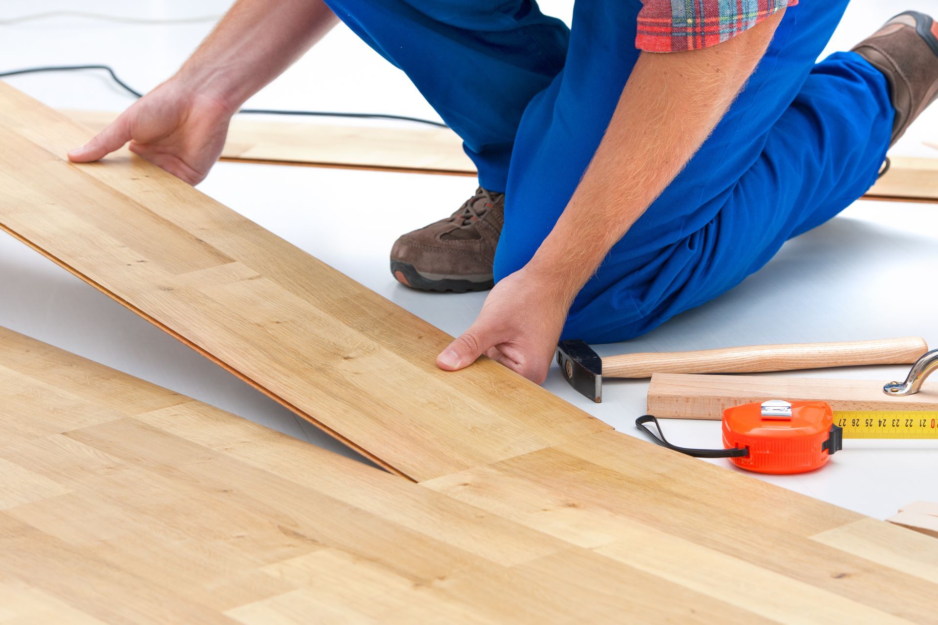 A man is kneeling down to install a wooden floor