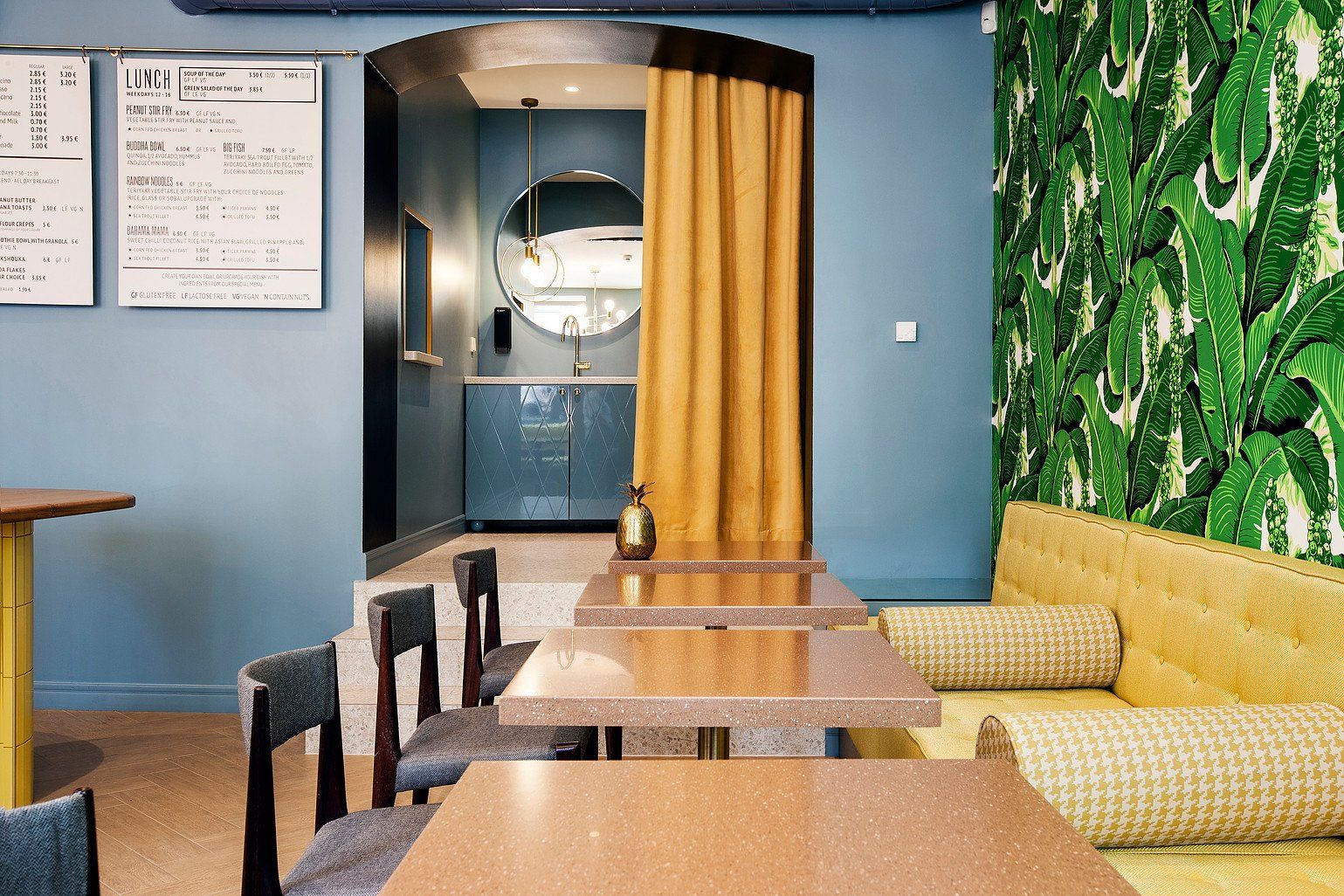 galdiņi ar krēsliem un zilu sienu, dzelteniem aizkariem