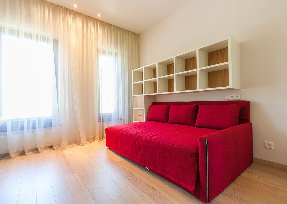 guļamistaba ar sarkanu gultu un sienas plauktiem