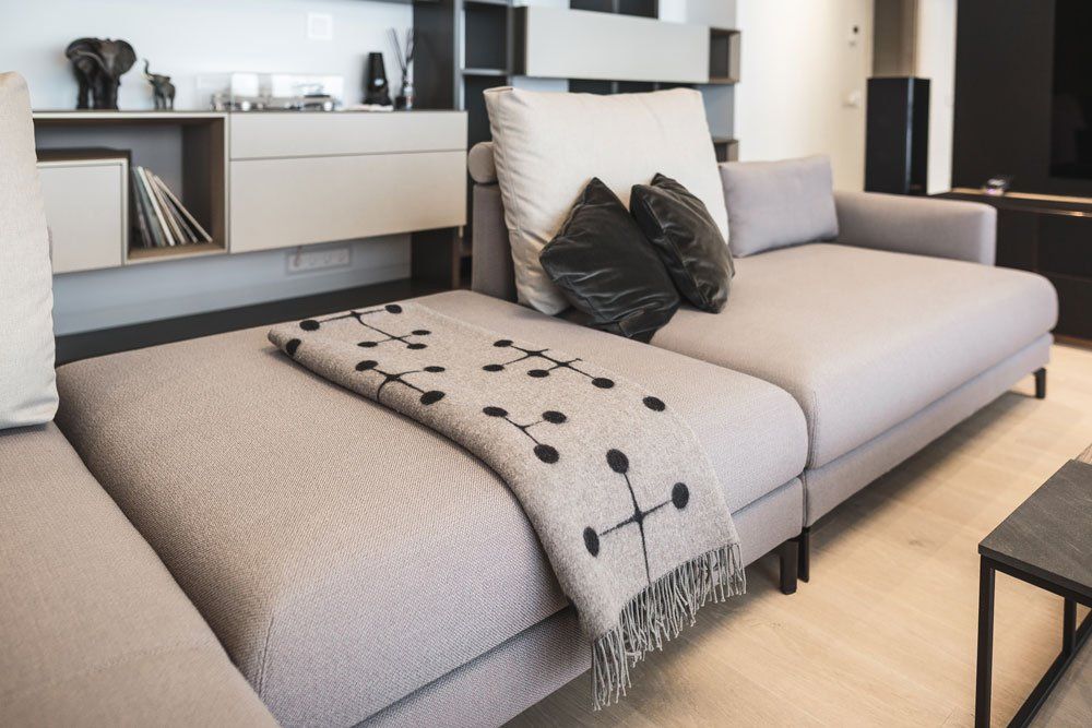 dīvāns ar pelēku segu un baltu spilvenu