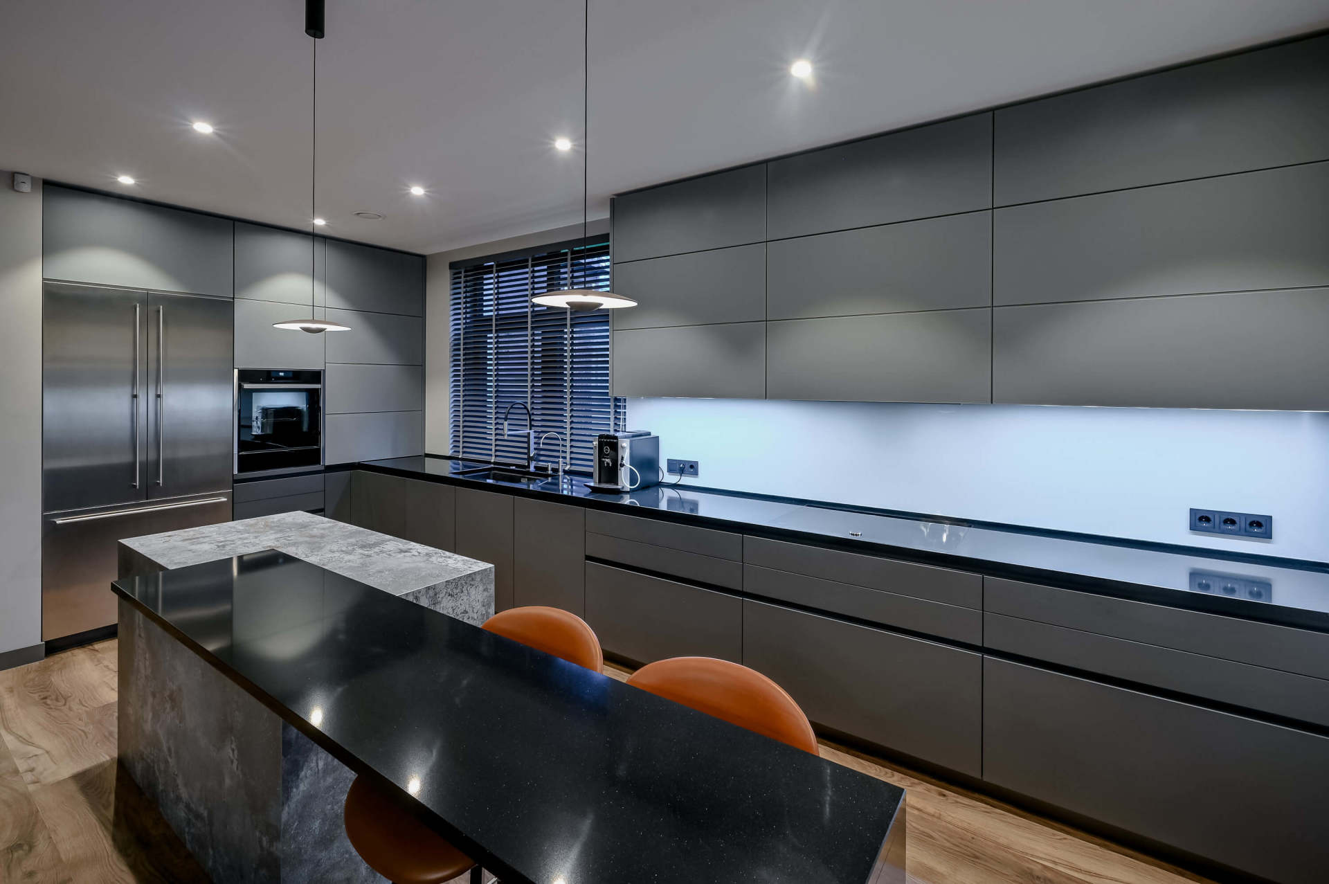 tumša virtuves tehnika un plaukti ar diviem oranžiem krēsliem
