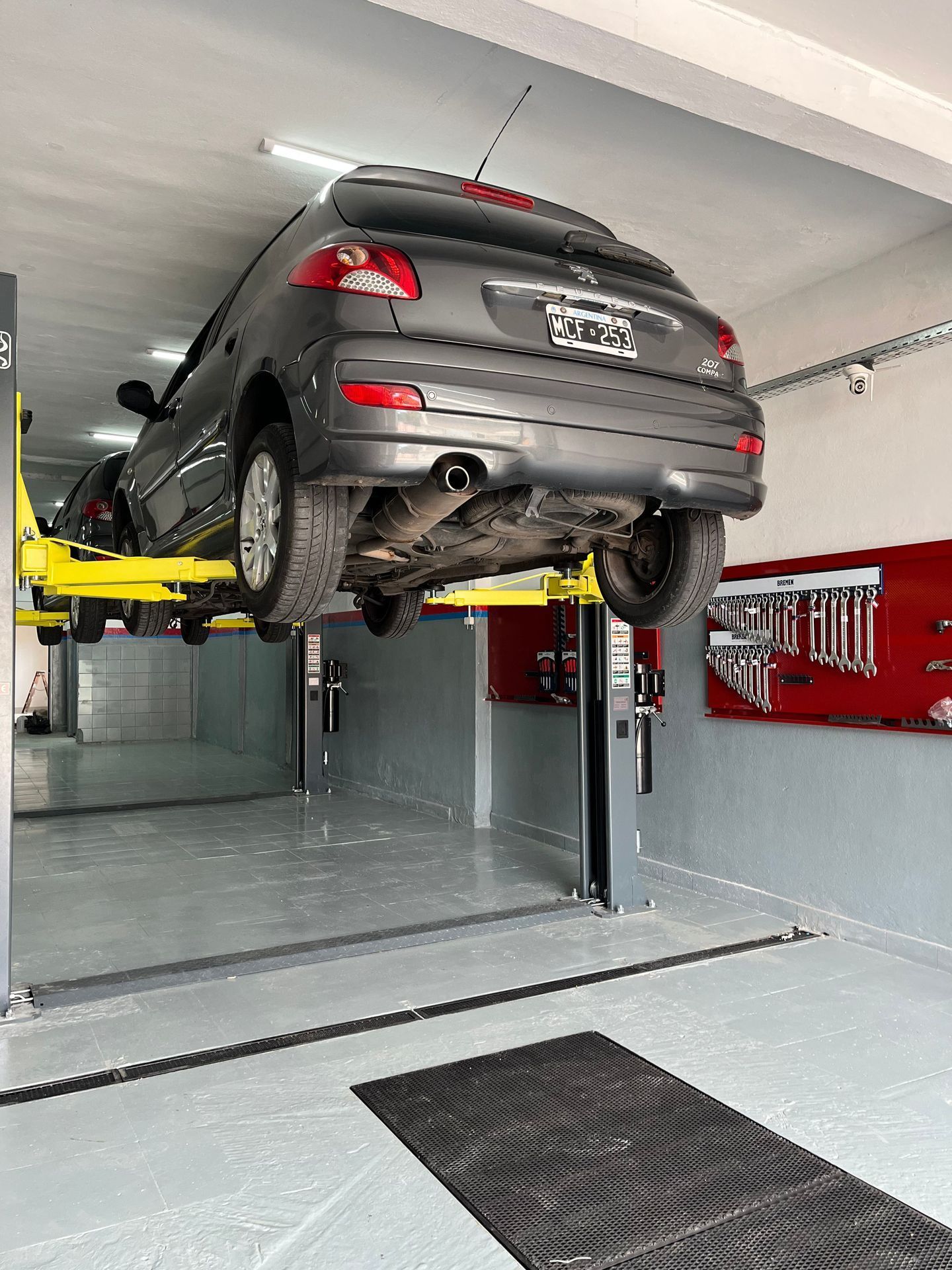 Un automóvil gris subido a un elevador amarillo en un taller de reparación de automóviles.