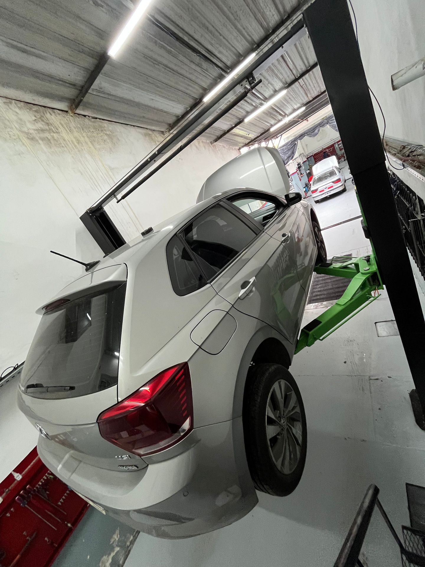 Coche plateado sobre un elevador verde en un taller de reparación, capó abierto, toma en ángulo.