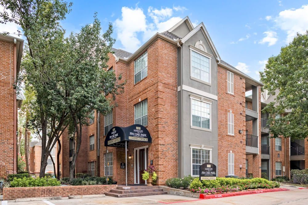 a large brick apartment building with a blue awning over the entrance at Marquis on Pin Oak in Houston, TX.