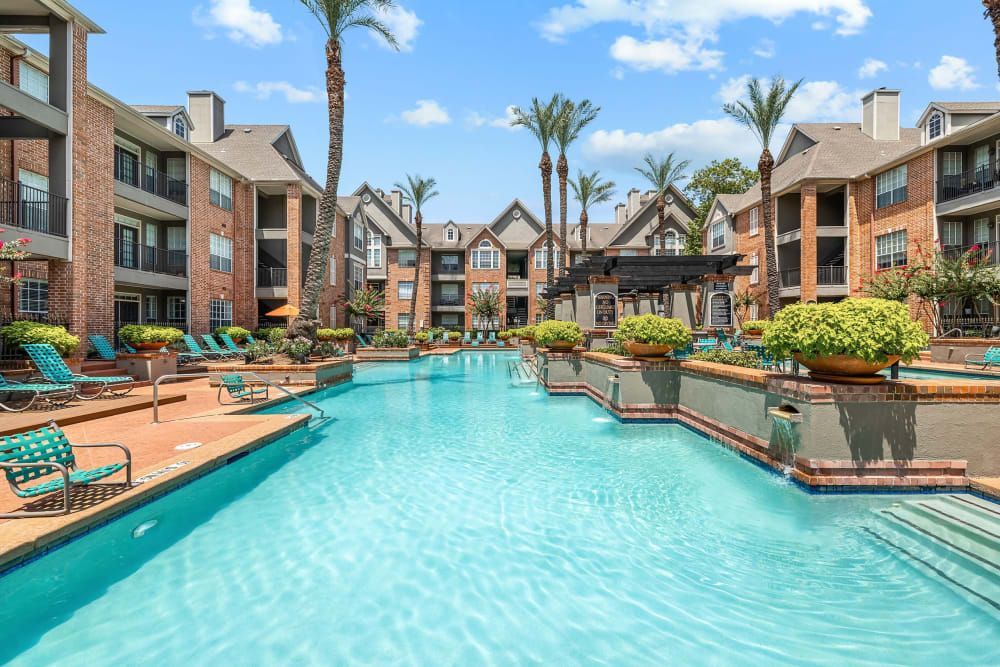a large swimming pool surrounded by palm trees in front of a building at Marquis on Pin Oak in Houston, TX.