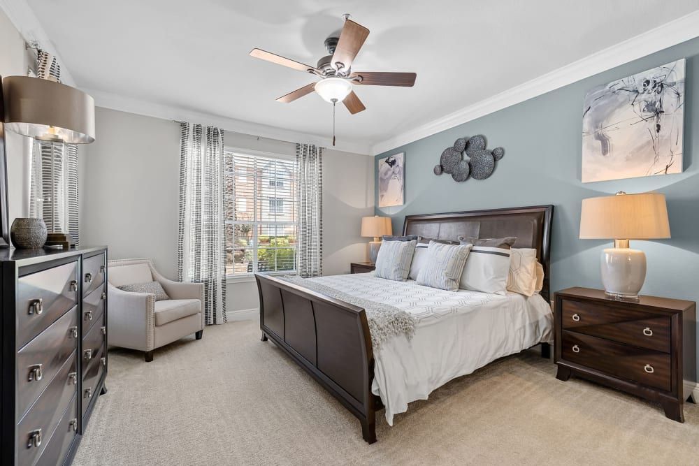 a bedroom with a king-size bed, dresser, nightstand, chair, and ceiling fan at Marquis on Pin Oak in Houston, TX.