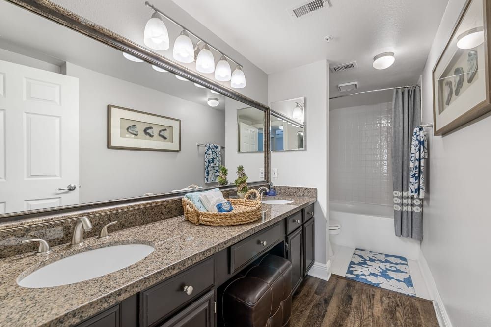 a bathroom with two sinks, a large mirror, and a walk-in shower at Marquis on Pin Oak in Houston, TX.