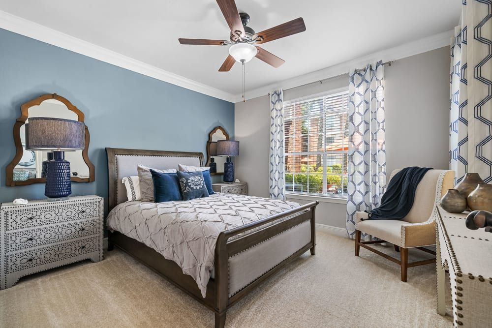 a bedroom with a bed, chair, dresser, and ceiling fan at Marquis on Pin Oak in Houston, TX.