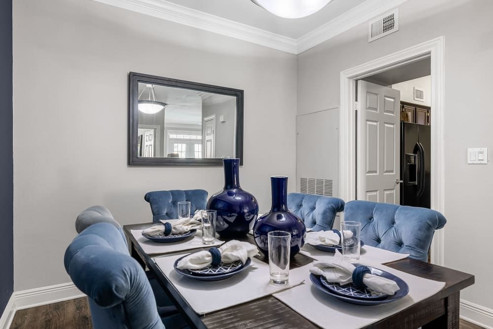 a dining room table with blue chairs and plates and glasses on it at Marquis on Pin Oak in Houston, TX.
