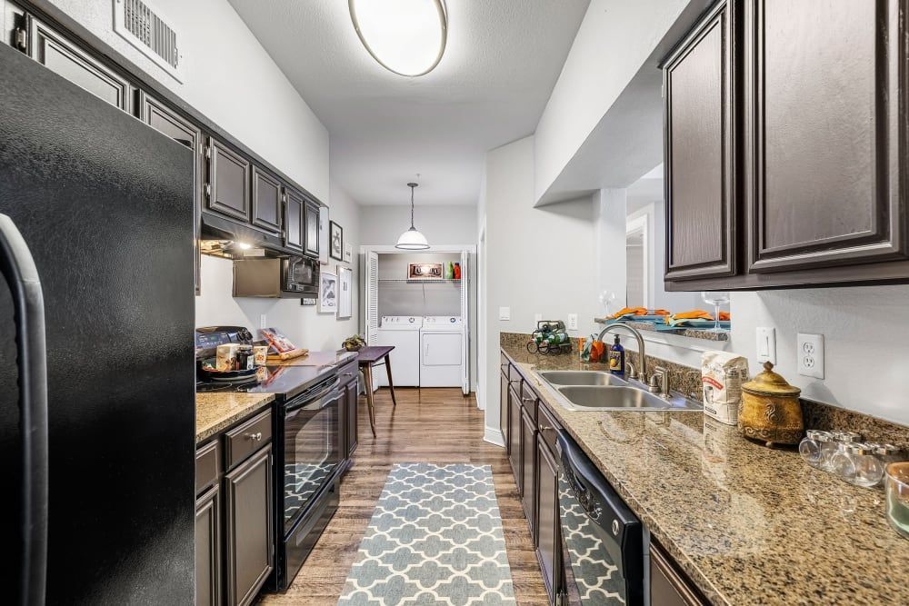a kitchen with granite counter tops, stainless steel appliances, and a black refrigerator at Marquis on Pin Oak in Houston, TX.