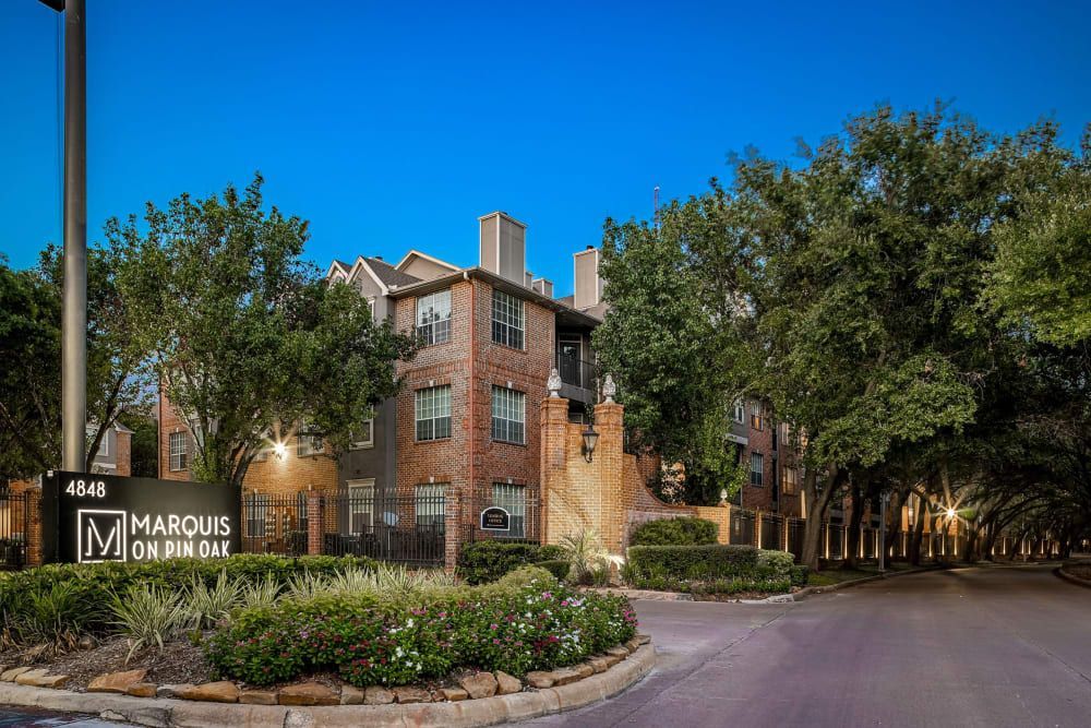 a large apartment building with a sign in front of it surrounded by trees and bushes at Marquis on Pin Oak in Houston, TX.