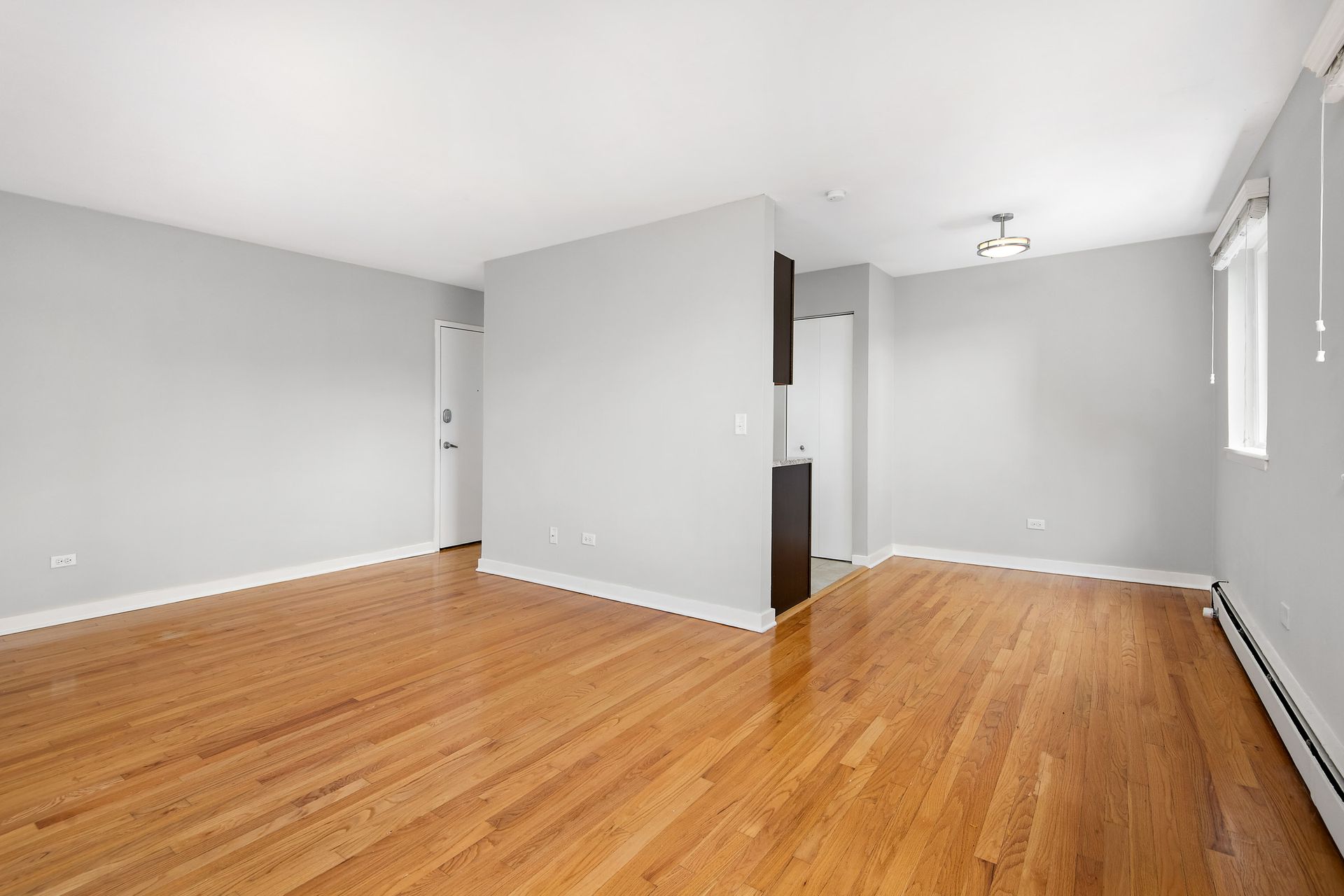 An empty living room with hardwood floors and white walls at Reside at 2727.