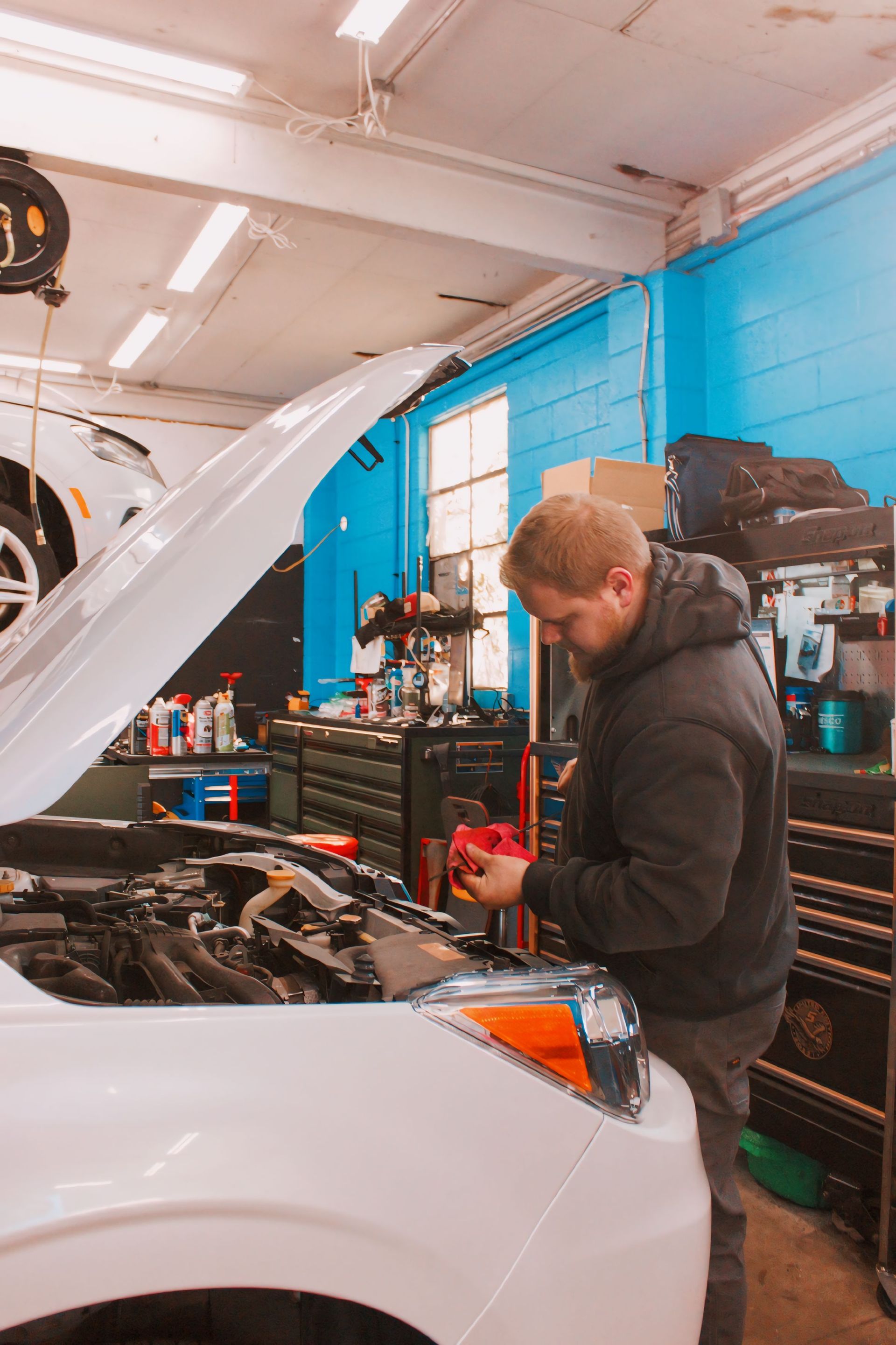 Mechanic working on a white car in a garage, checking fluid levels under the hood.