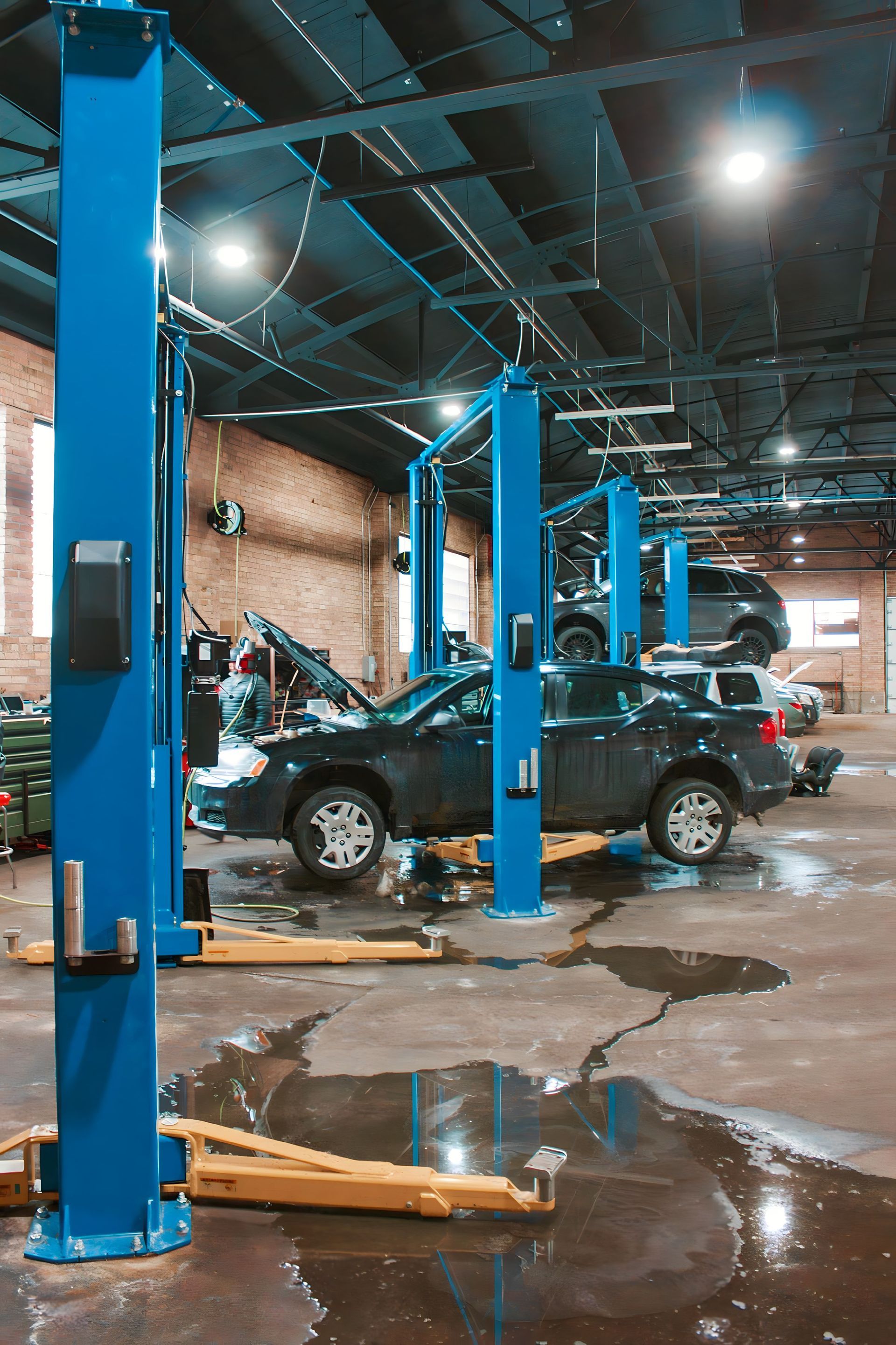 A car repair shop with multiple cars on lifts. Blue lifts, wet floor, brick walls.