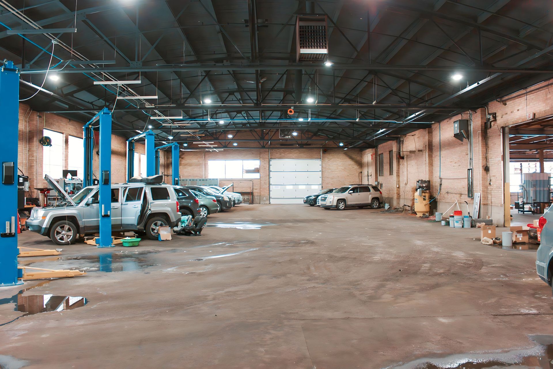 Interior of a car repair shop with multiple vehicles on lifts and service bays. Blue lifts, concrete floor, and high ceiling.