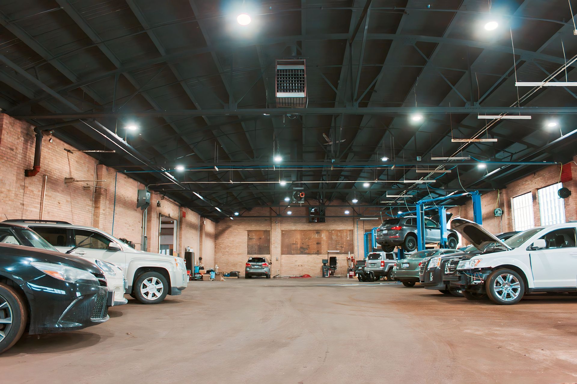 A car repair shop with several cars in various stages of repair. The ceiling is industrial with bright lights.