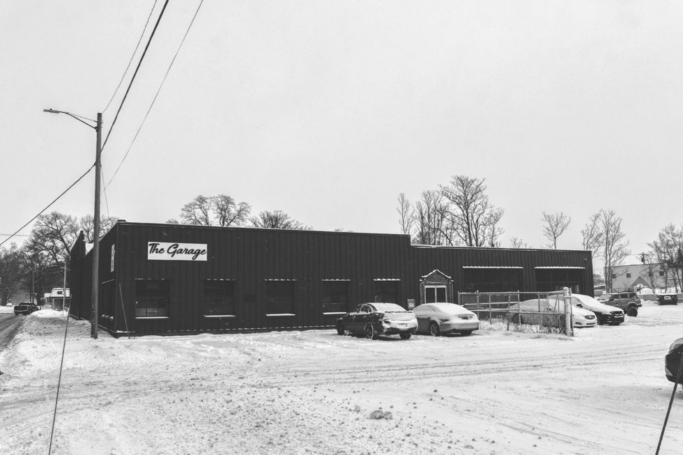 Black and white photo of The Exchange, a dark building in a snowy landscape, cars parked out front.