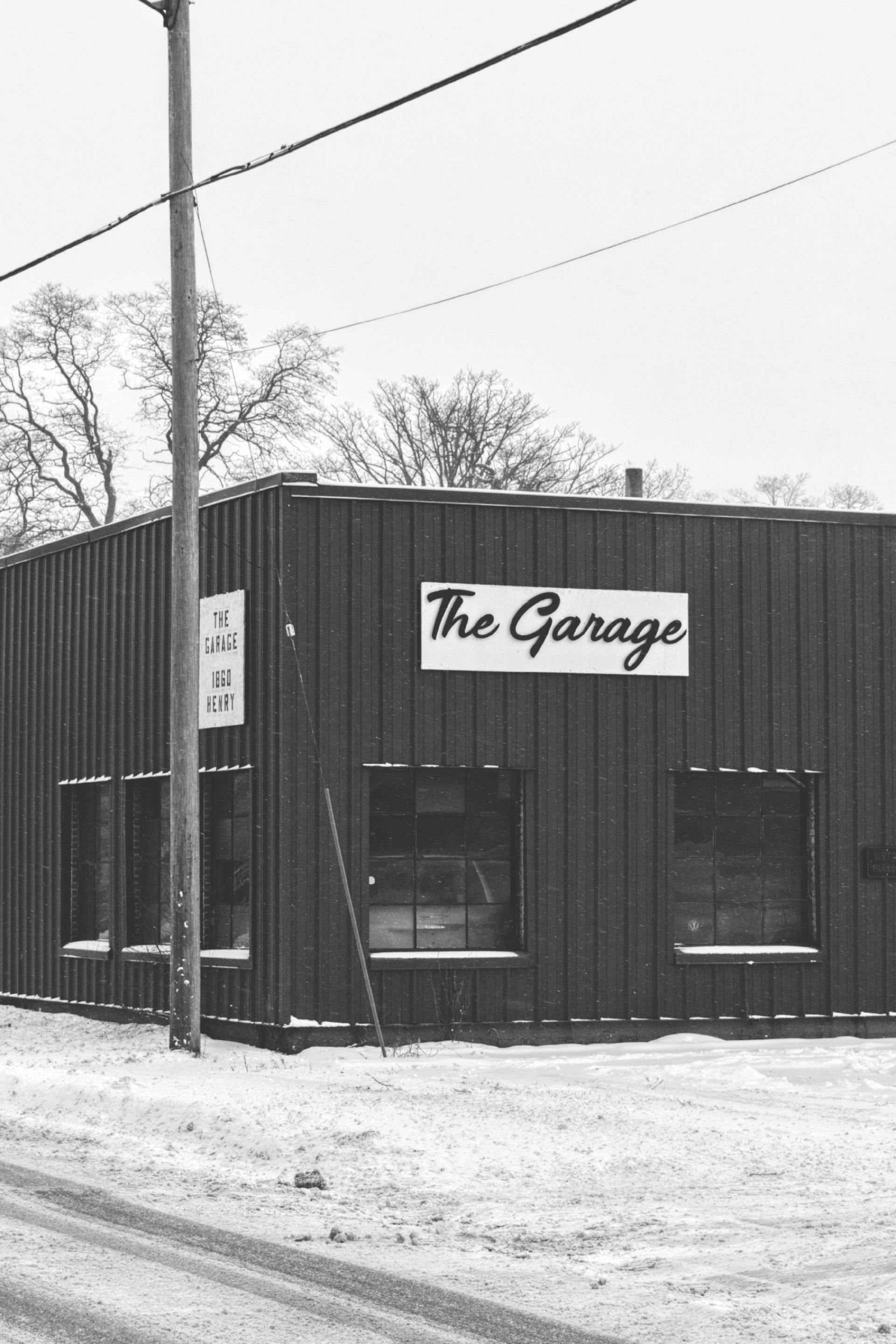 Black and white photo of a garage in the snow; a sign says 