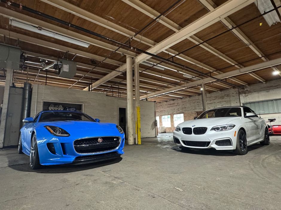 A blue Jaguar F-TYPE and a white BMW 2 Series parked inside an industrial building.