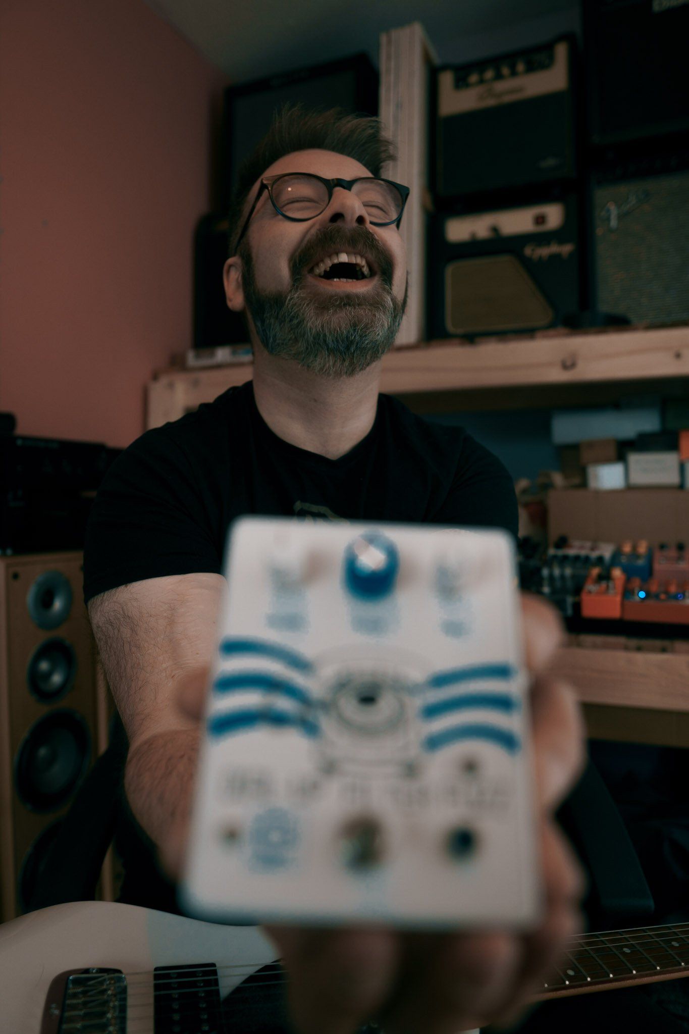 man with beard and glasses holding guitar pedal and laughing