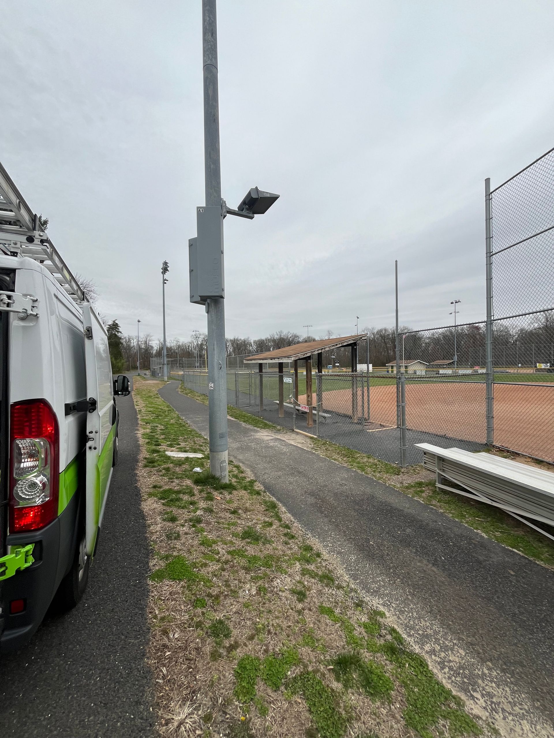 A van is parked on the side of the road next to a baseball field.