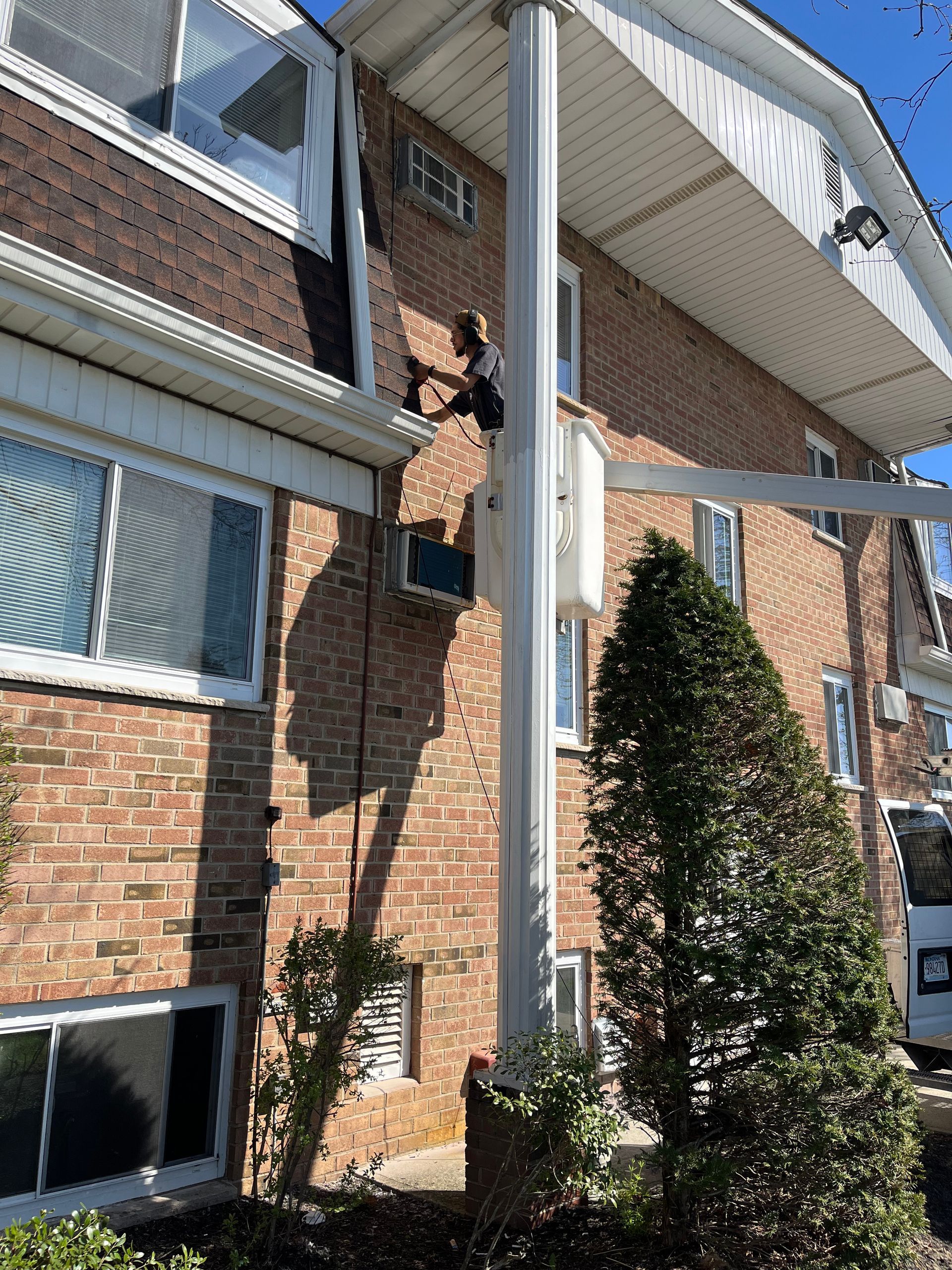 A man is standing in a bucket on the side of a brick building.