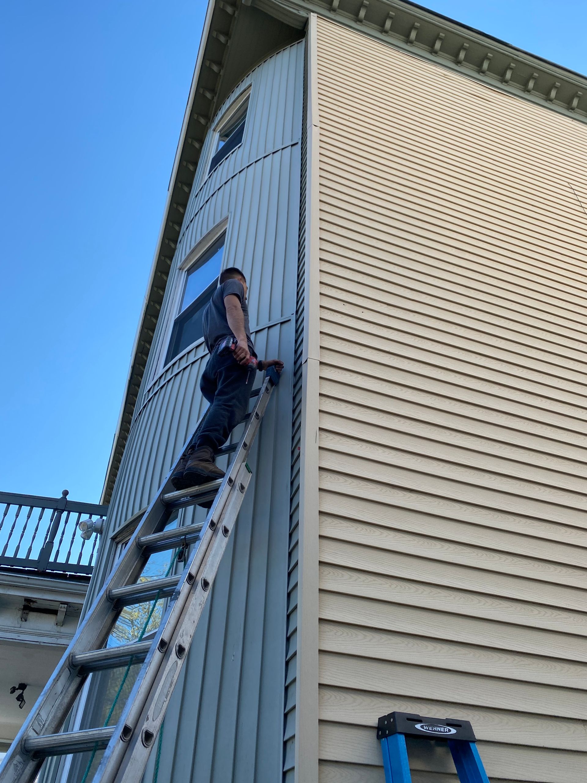 A man is standing on a ladder on the side of a house.