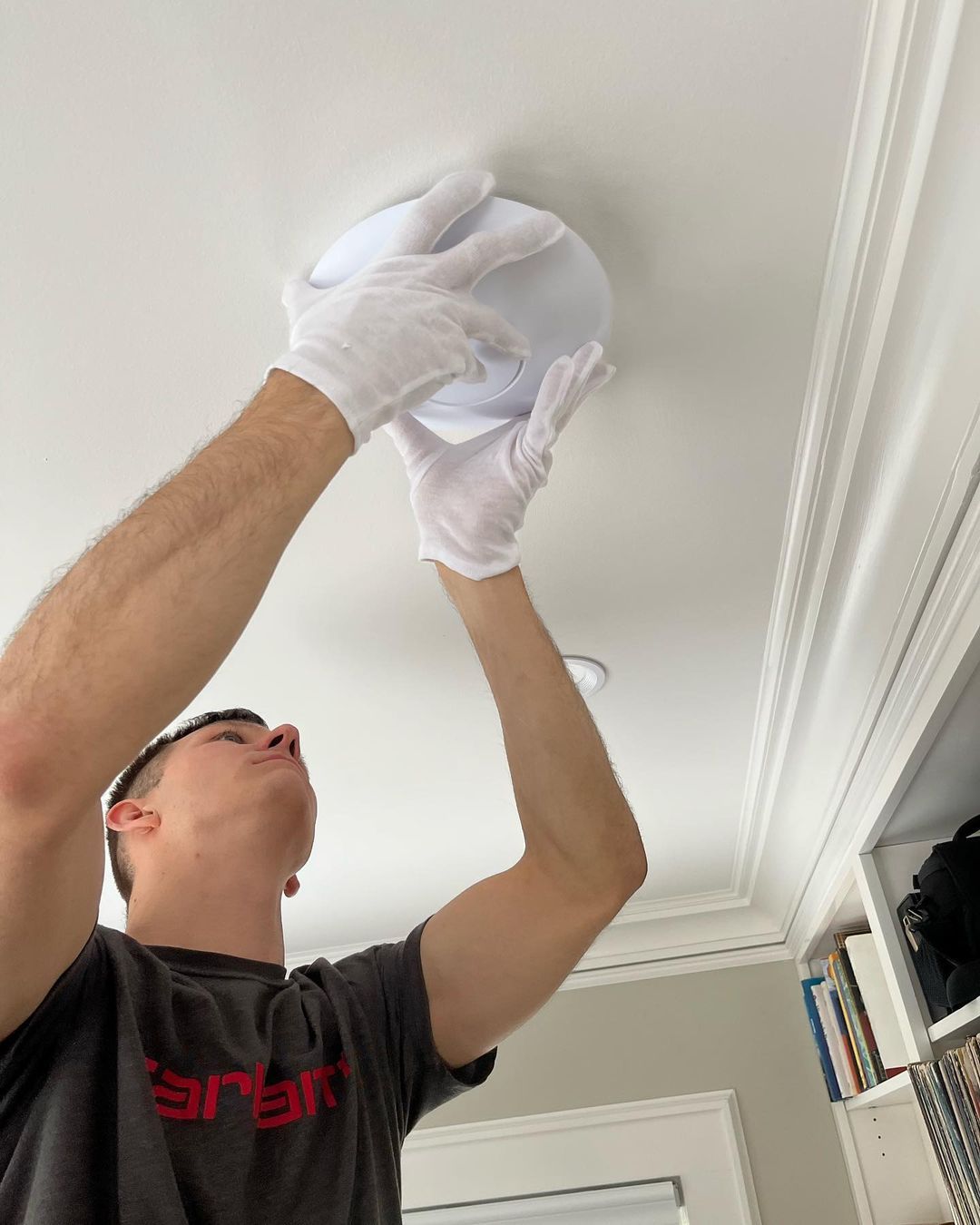 A man wearing white gloves is reaching for a light on the ceiling.
