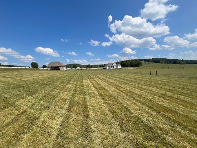 A large grassy field with a barn in the background on a sunny day.