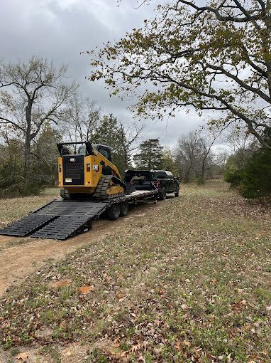 A truck is towing a bulldozer on a trailer in a field.