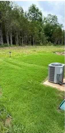 An air conditioner is sitting in the middle of a lush green field.